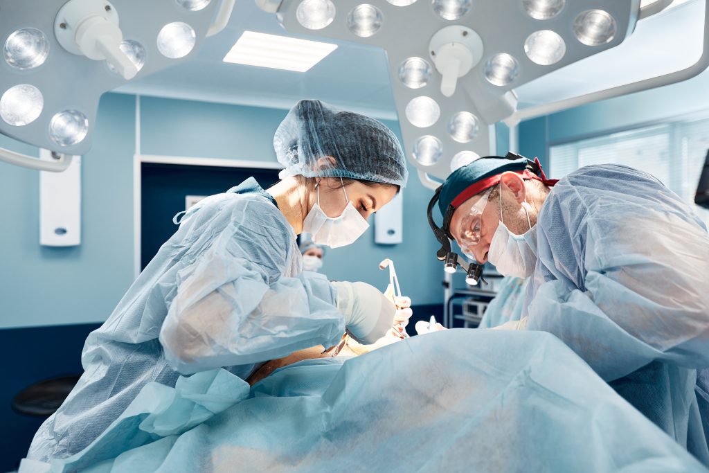 Surgeons in a light operating room perform plastic surgery, a team of male and female doctors perform reconstructive surgery – Alpha Hospital Group